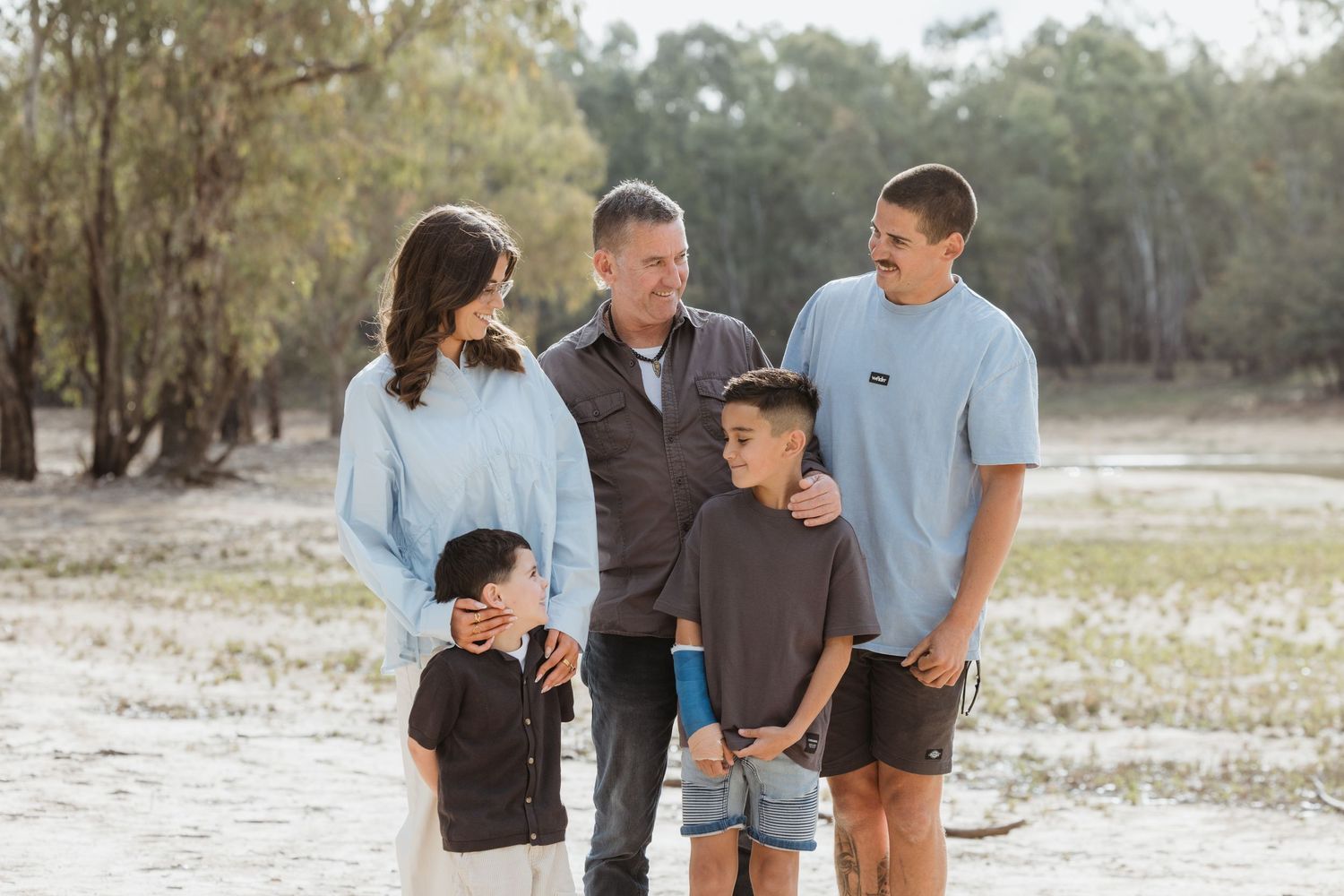 A family in coordinating blue and brown outfits walks together through a scenic outdoor setting during a photo session.