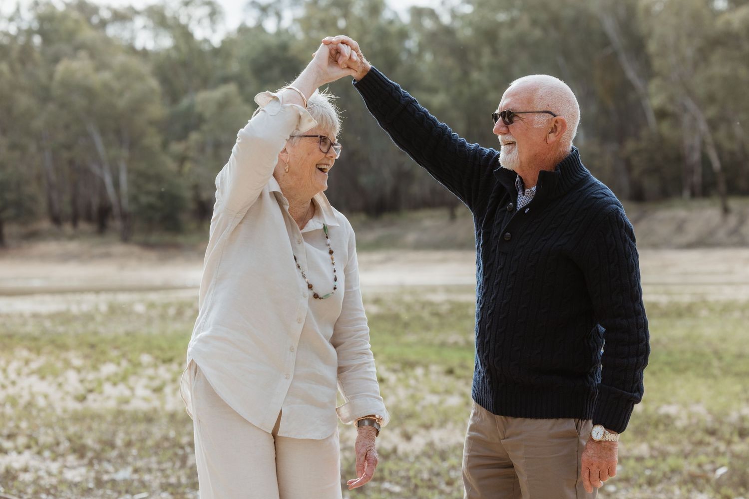A couple shares a romantic moment outdoors in a field with wildflowers and trees in the background.