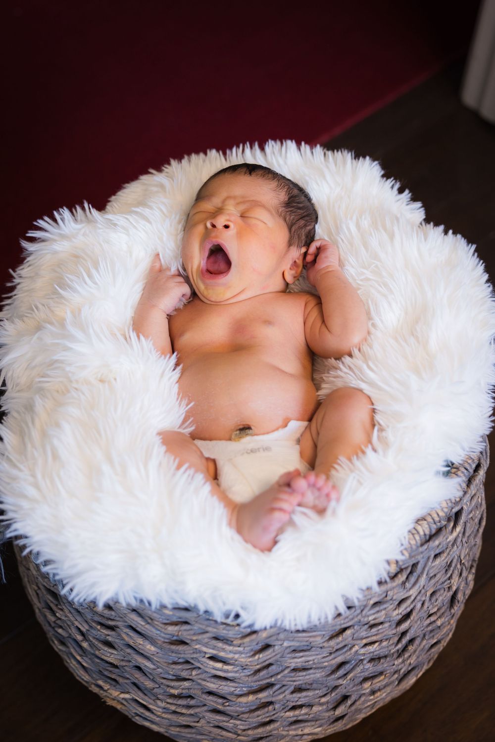 A tiny reclining baby nestles peacefully in a cozy woven basket lined with fluffy white faux fur.