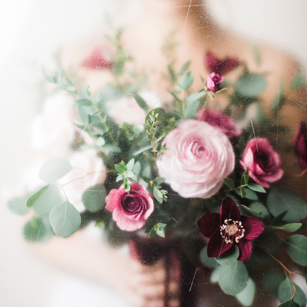 Bride holding a romantic bouquet of pink paper ranunculus, burgundy paper roses, and eucalyptus greenery.