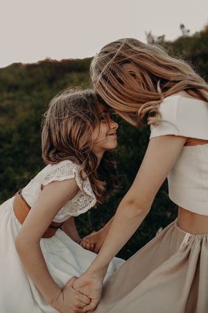 Two people in white dresses share an intimate moment outdoors at dusk with windswept hair.