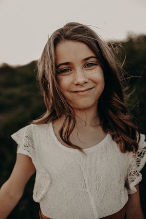 Portrait of someone wearing a white lace top with short sleeves smiling warmly at the camera in natural lighting.