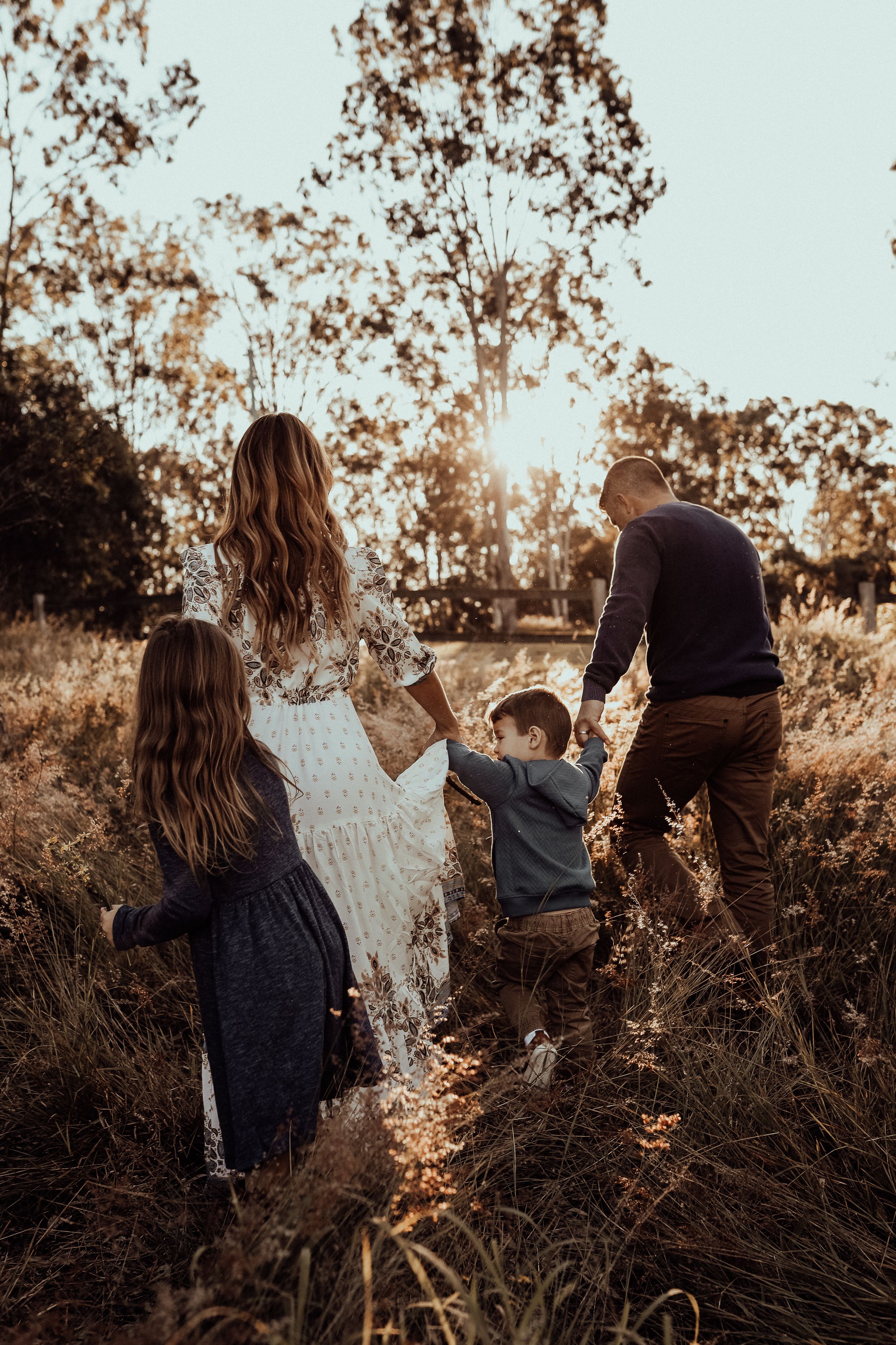 A family walks together through tall golden grass during sunset in a rural field.
