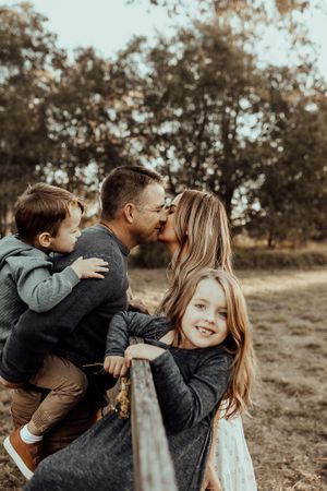 A loving family shares a tender moment together while leaning against a rustic wooden fence at sunset.