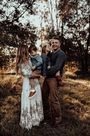 A family poses together in a serene outdoor setting at golden hour with tall trees in background.