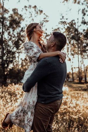 A couple embraces romantically in a sunlit field during golden hour.