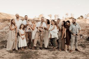 A wedding party poses together outdoors wearing coordinated neutral-toned outfits against a desert landscape.
