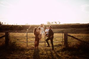 Silhouettes of three people leaning on a rustic wooden fence at golden hour in a countryside setting.
