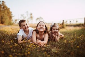 Three kids lie in a golden meadow during sunset, laughing and enjoying the outdoors together.