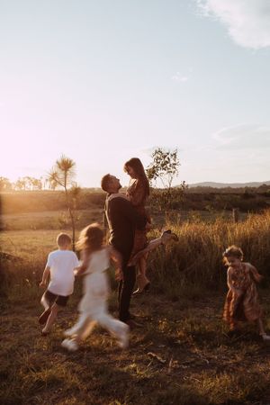 Children and adults playing together in a golden field at sunset with mountains in the background.