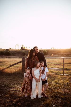 Sunset silhouettes family in rustic countryside setting with wooden fence and glowing warm light.