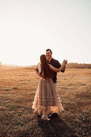 Couple dancing in an open field during sunset with warm golden light.