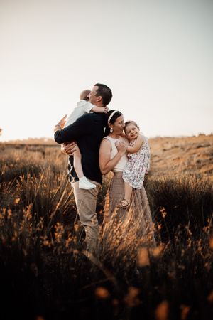 Golden hour family portrait in tall grass field with warm lighting.