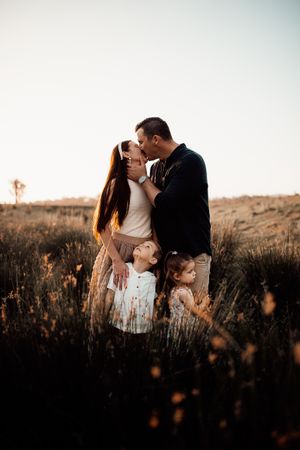 Intimate family moment captured in tall grass during golden hour sunset.