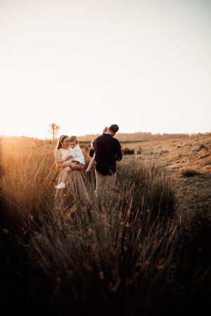 Family walking through golden grass field at sunset with backlit warm tones.