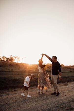 Family dancing together on dirt path during golden sunset with joyful expressions.