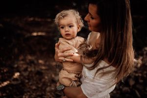 An intimate parent-child moment captured in a dark, moody forest setting.