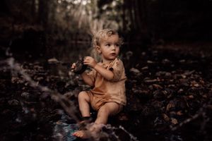 Drama toddler portrait in a dark moody forest setting with brown tones and fallen leaves.