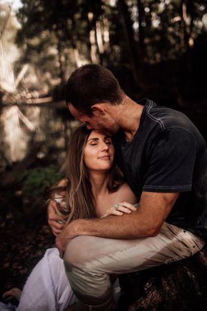 Intimate romantic portrait in warm moody forest setting during golden hour.