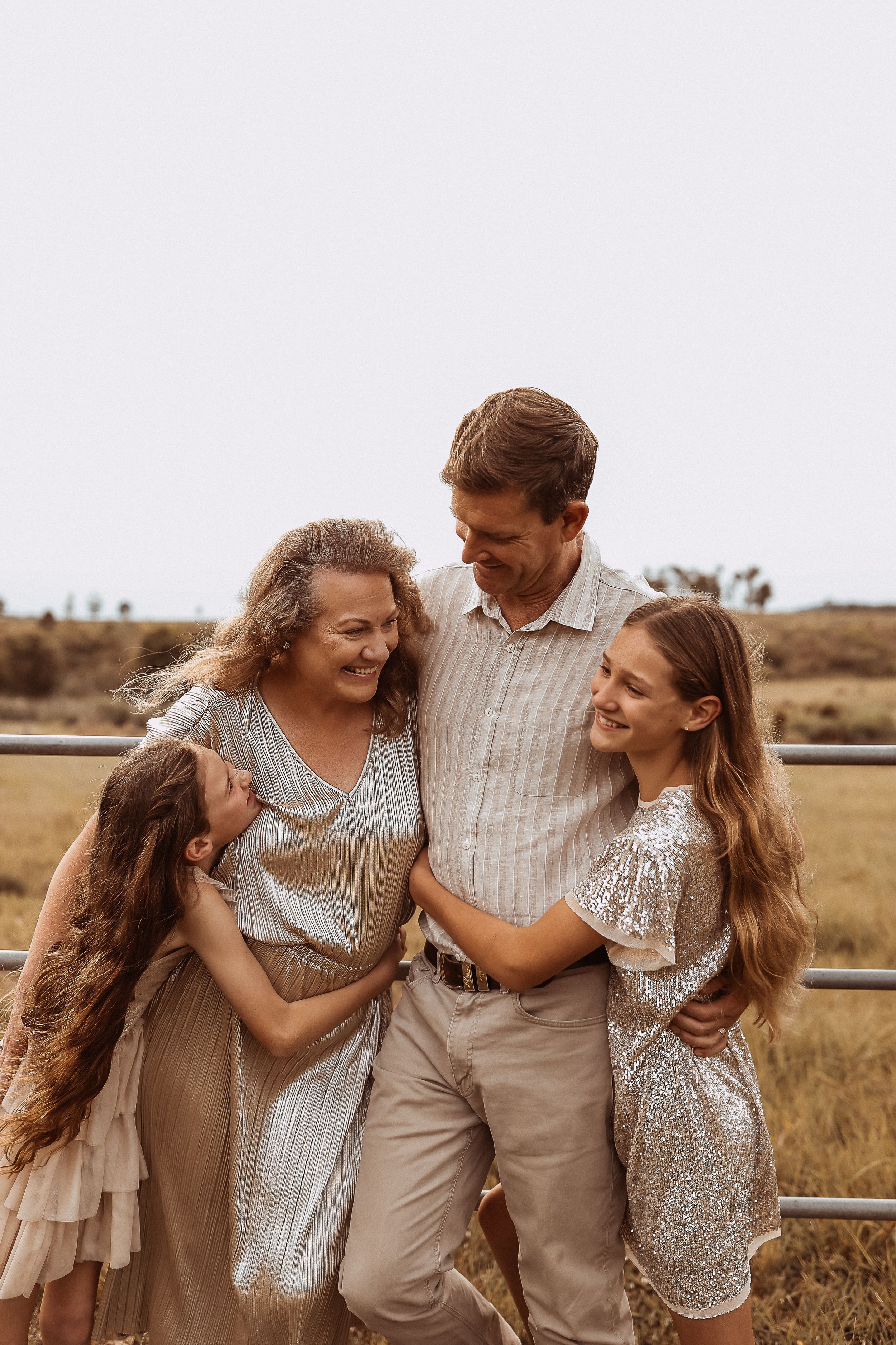 A loving family shares a candid moment together in a rustic field setting, wearing coordinated neutral-toned outfits.