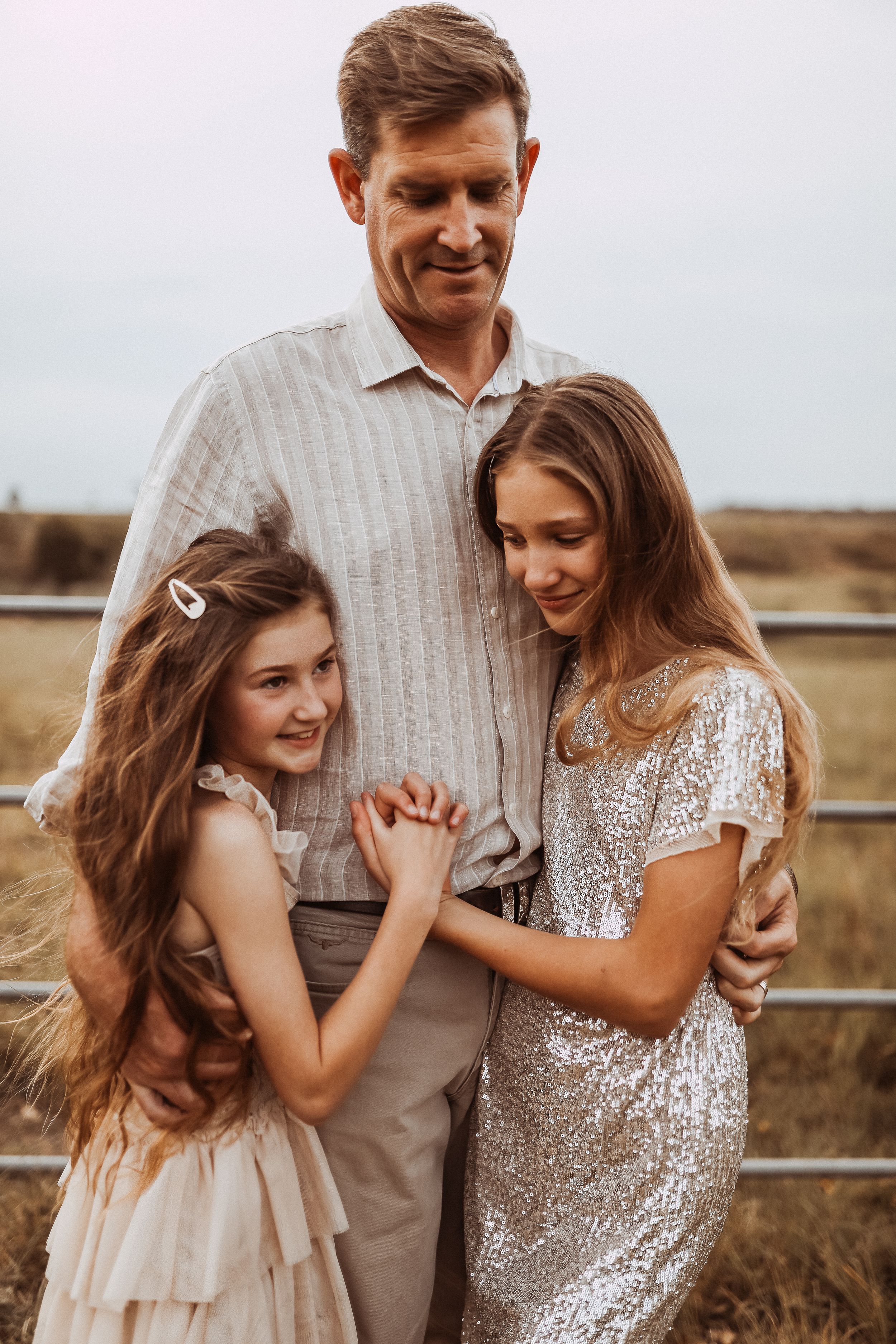 A happy family shares an intimate candid moment together outdoors at sunset against a rustic fence background.