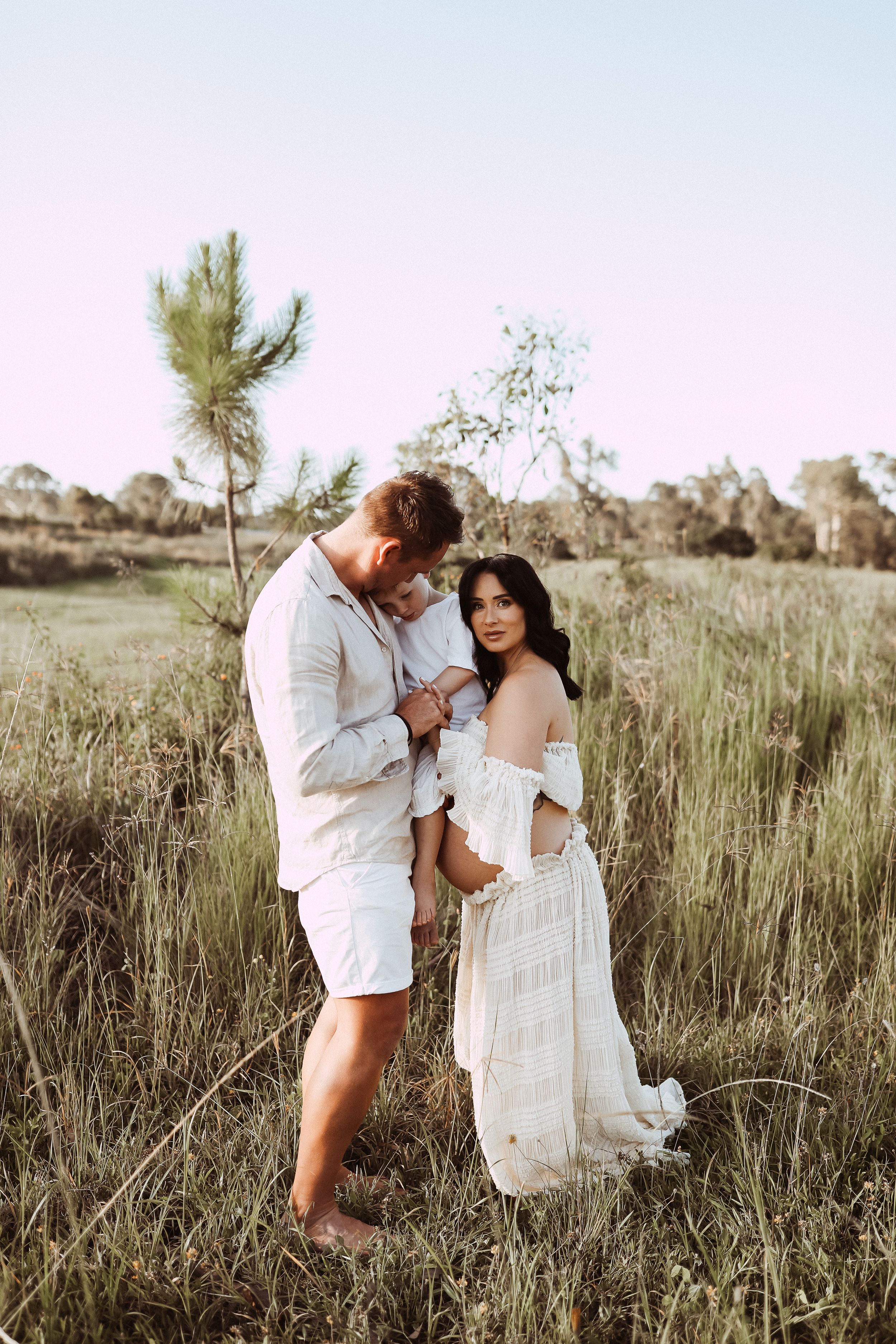 Romantic couple shares intimate moment in natural field setting during golden hour.