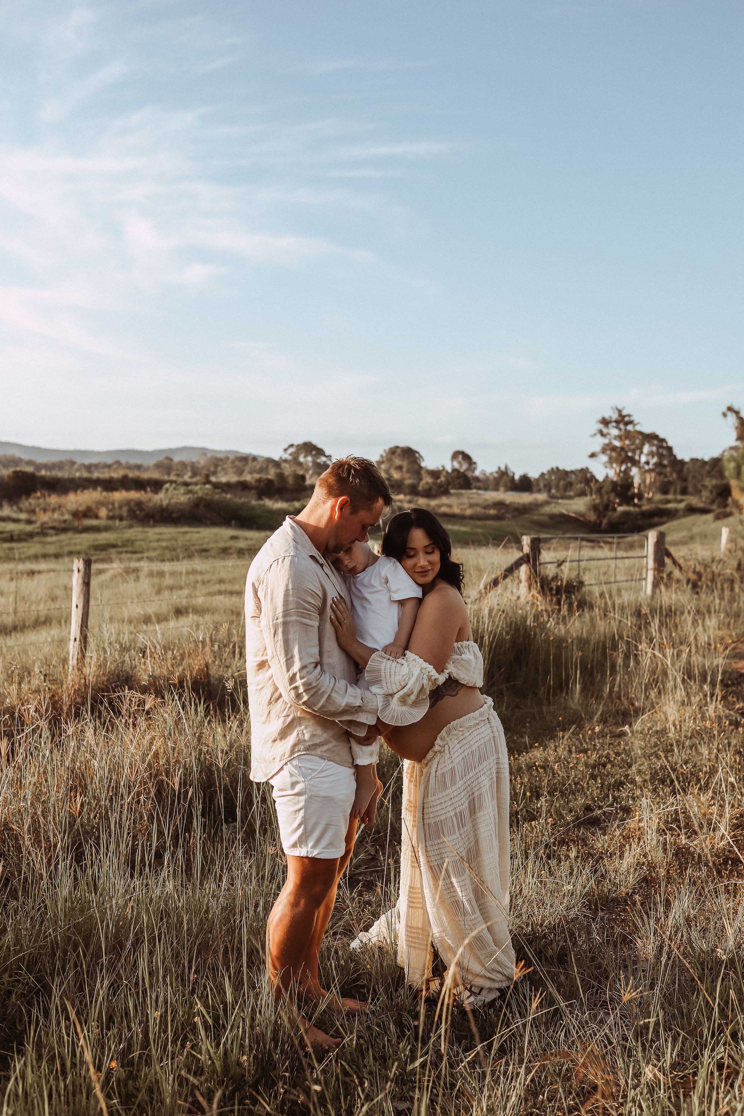 Tender moment captured between couple in countryside field with mountains in background.