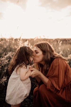 A tender outdoor moment at sunset shows a mother and daughter sharing an intimate kiss in a field of flowers.