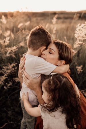 Loving embrace between family members in a sunlit field at golden hour with wildflowers in the background.