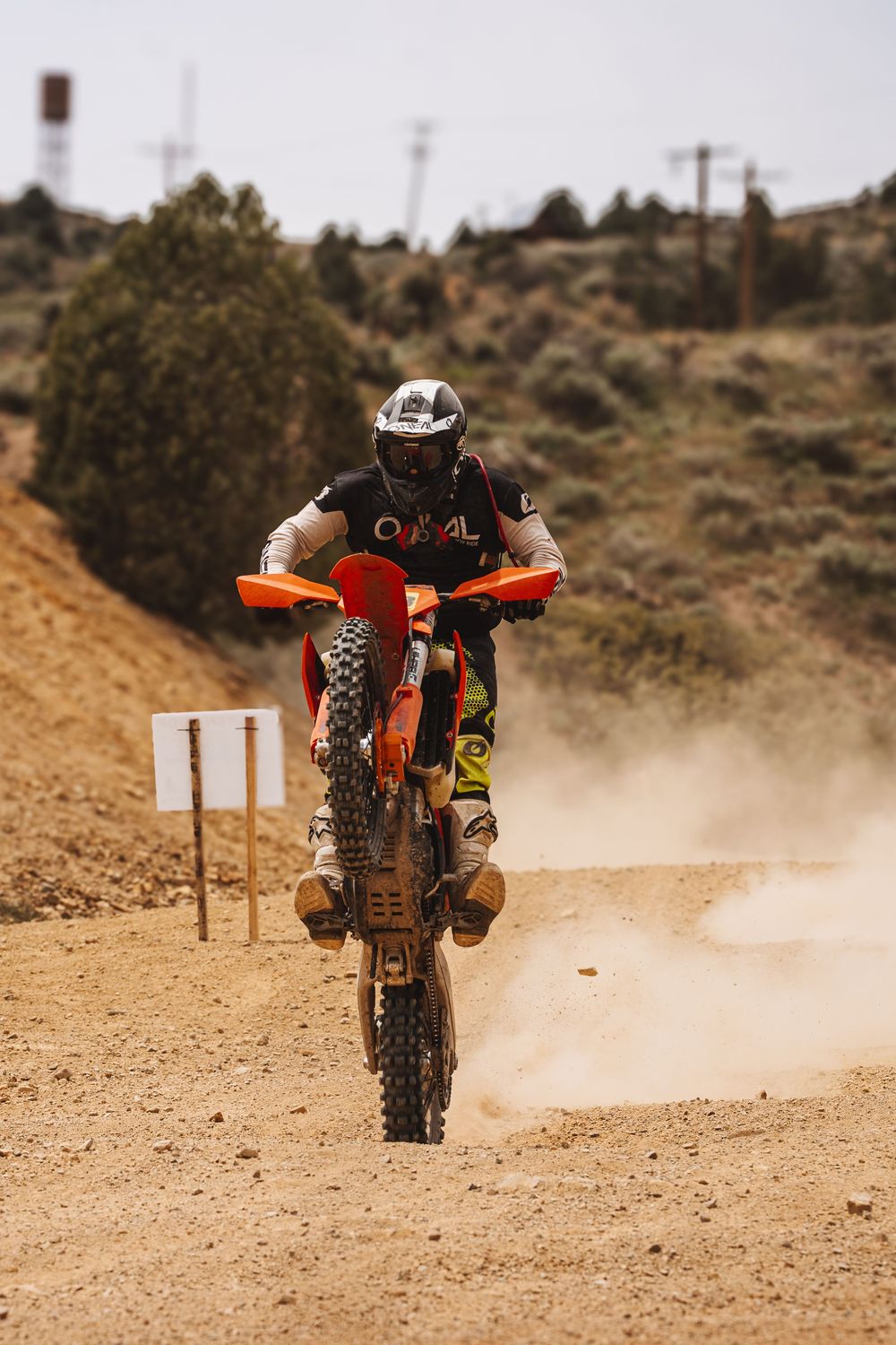 A motocross rider on an orange KTM dirt bike performs a wheelie on a sandy off-road track.