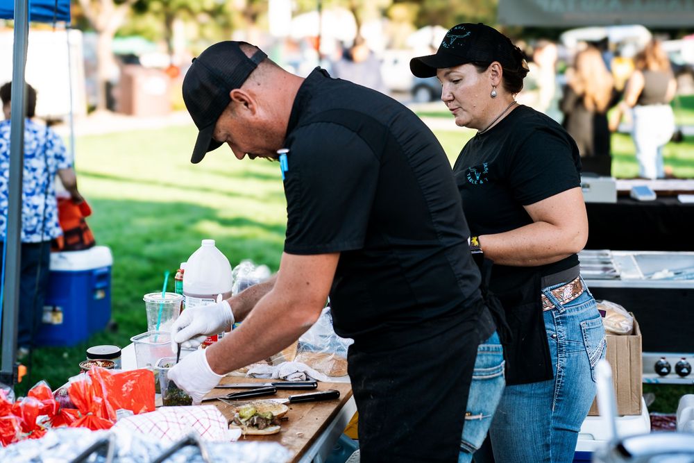 Food vendors prepare meals at outdoor event under white tents.