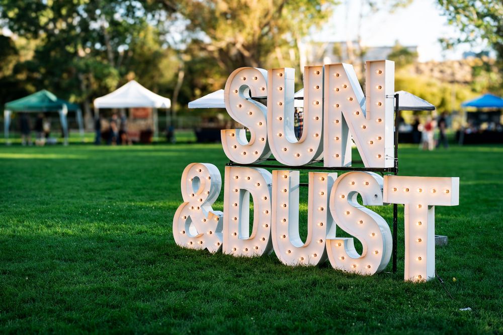 Large decorative letter signs spell out text on grassy lawn at outdoor event.