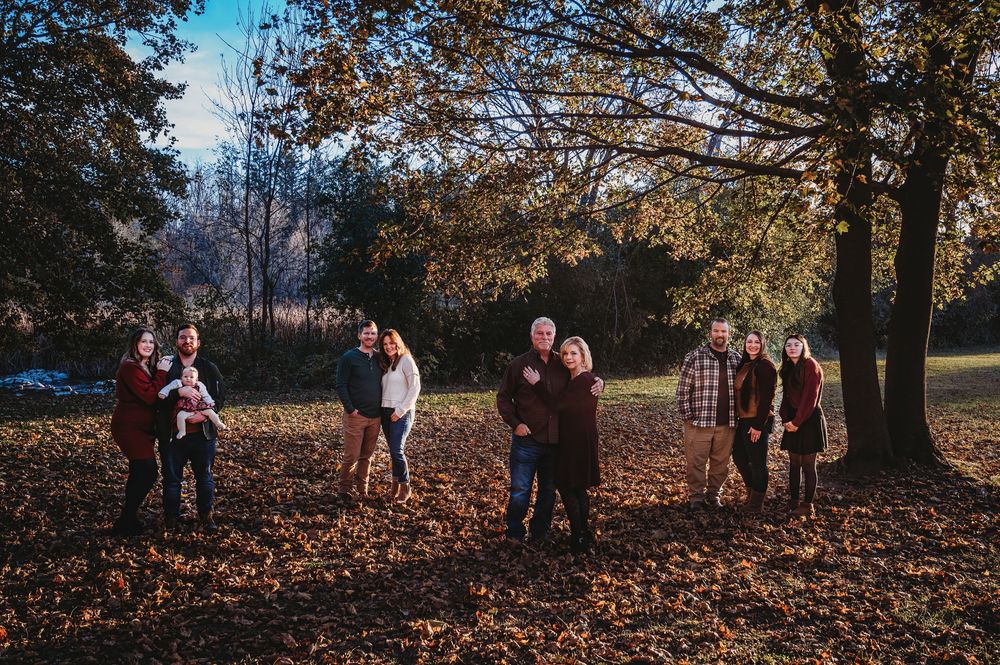 Family photoshoot in park with autumn leaves scattered on ground.