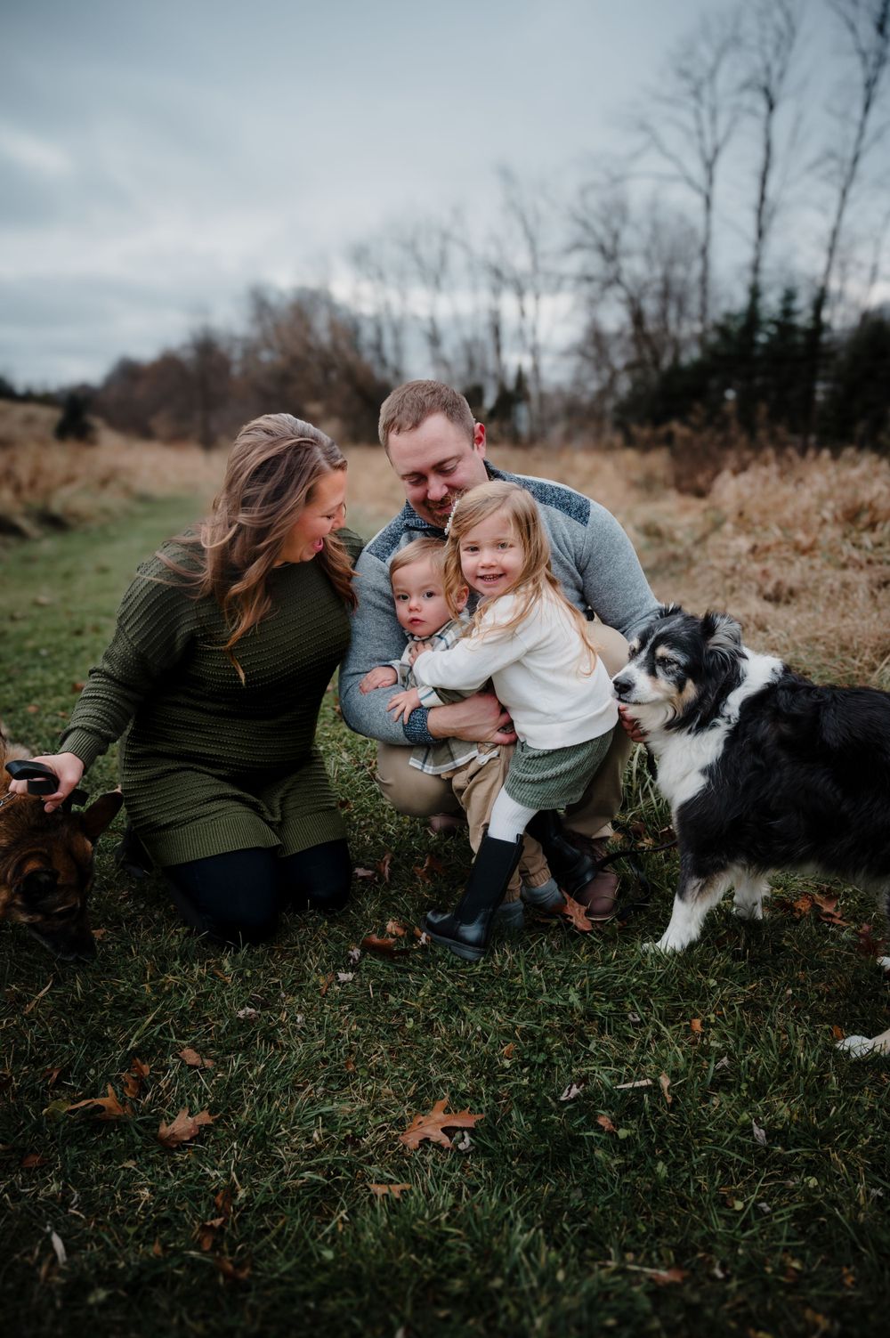 Family and dog share playful moment together on autumn grass with fallen leaves.