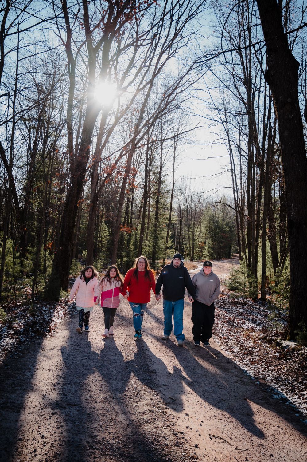 Group walking along forest path with dramatic sunlight casting long shadows through bare winter trees.