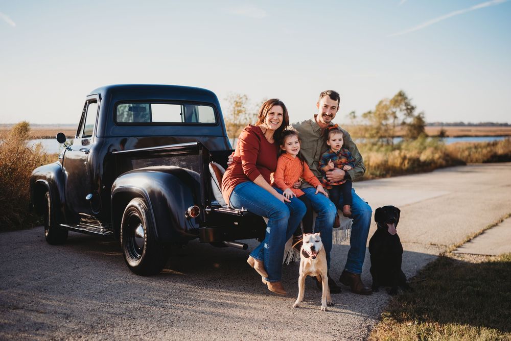 Couple poses with their dog next to vintage black truck on dirt road.
