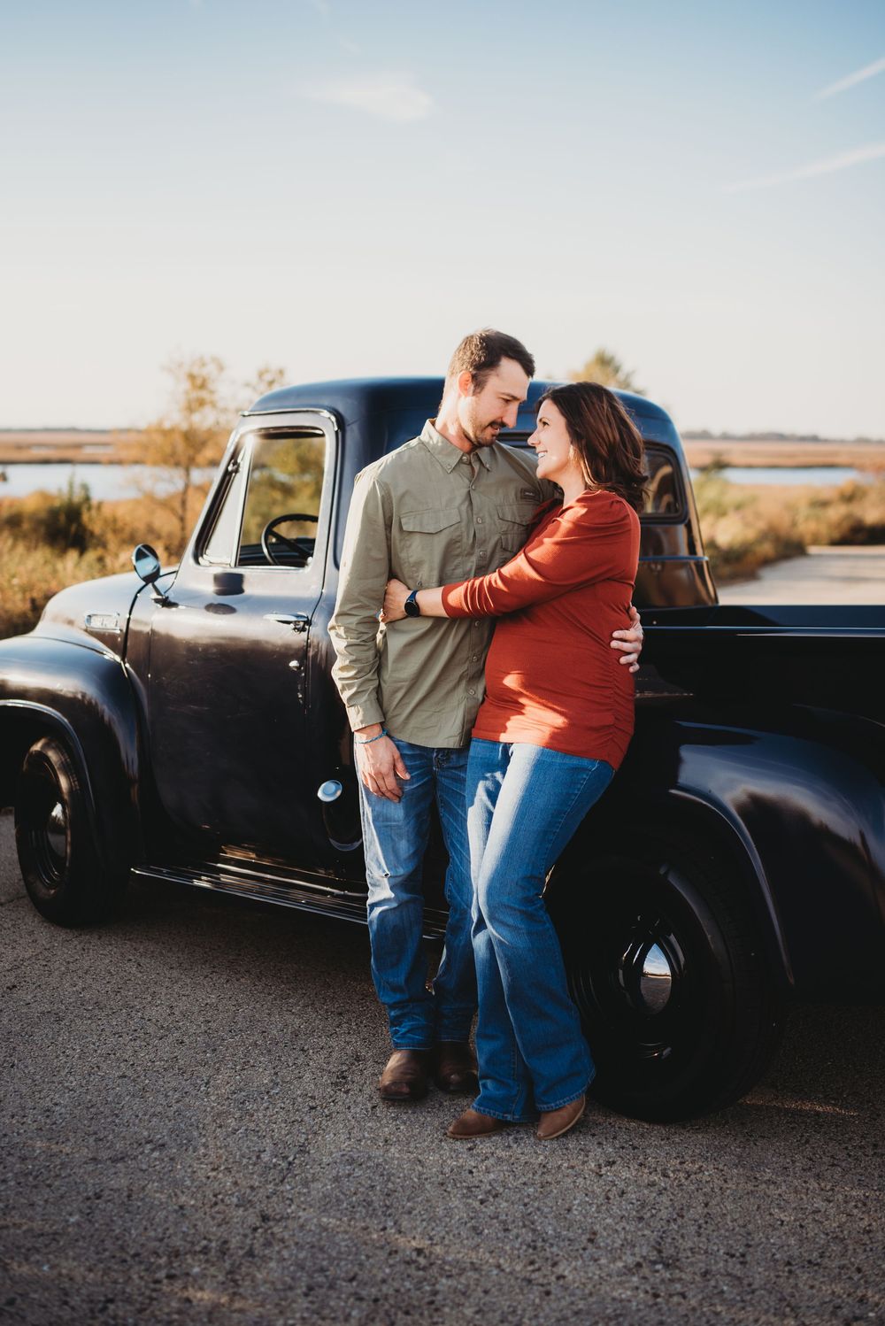 Romantic couple embracing against classic black pickup truck at sunset.