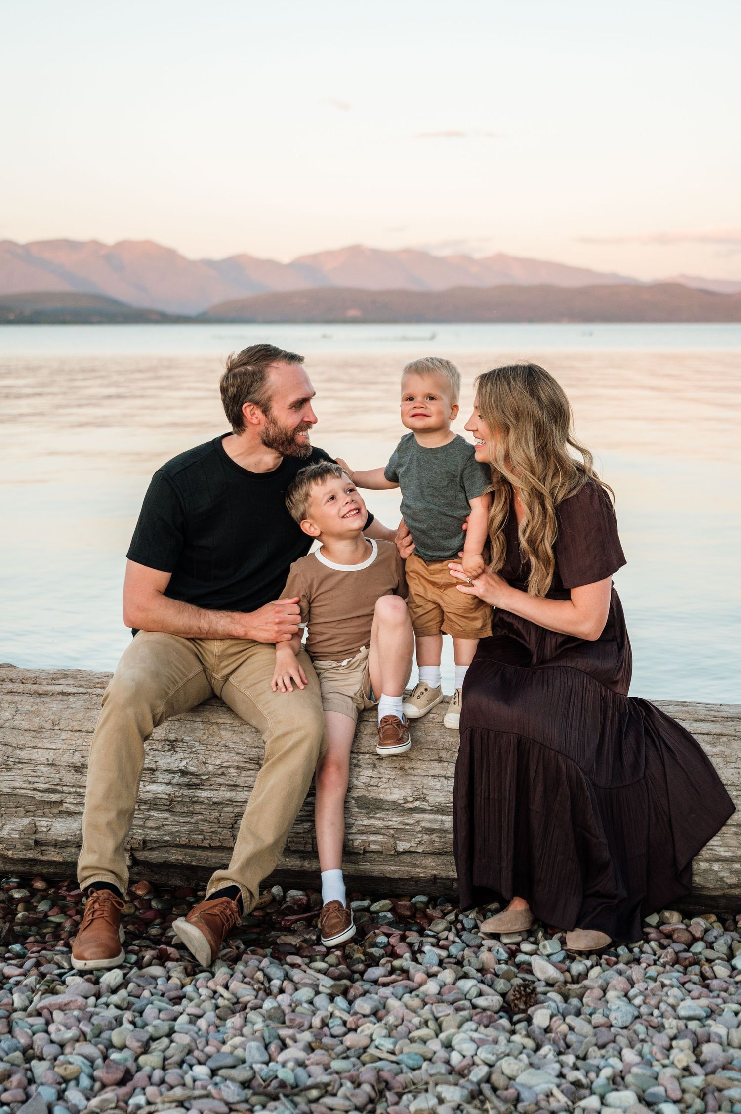 A family stands together with their dog on a rocky path during golden hour sunset with autumn trees in the background.