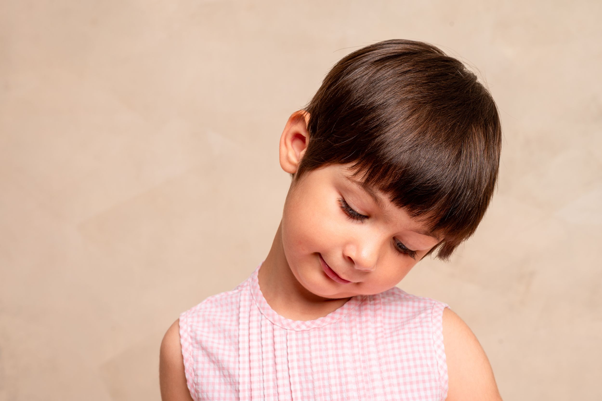 A child in a pink gingham dress leans down to examine something with curiosity.
