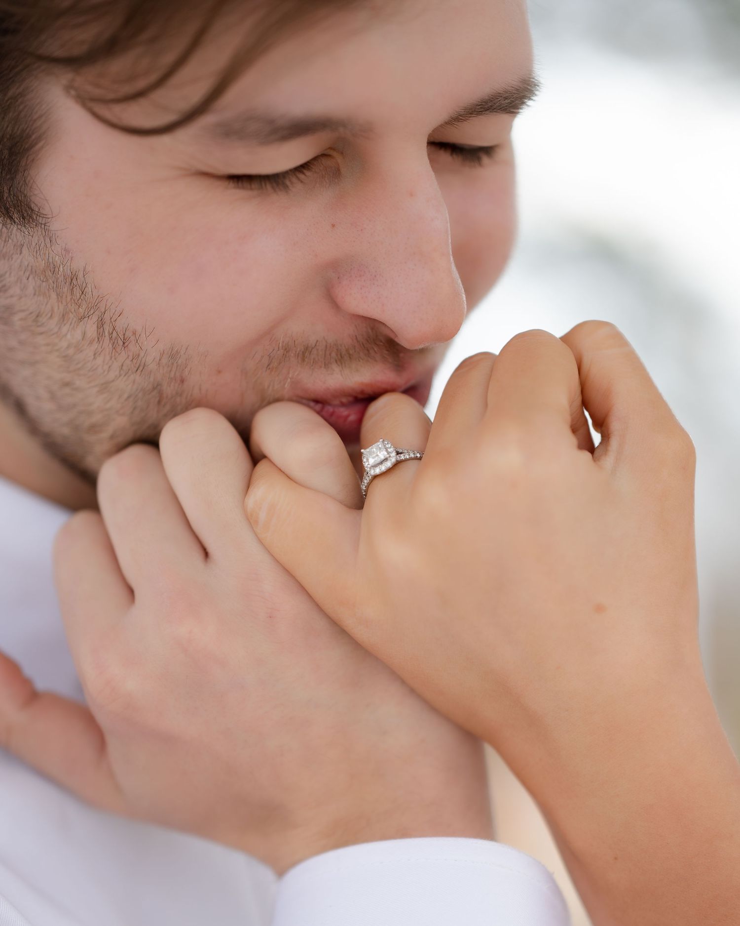 Close-up shot of someone tenderly kissing a hand with an engagement ring in soft lighting.