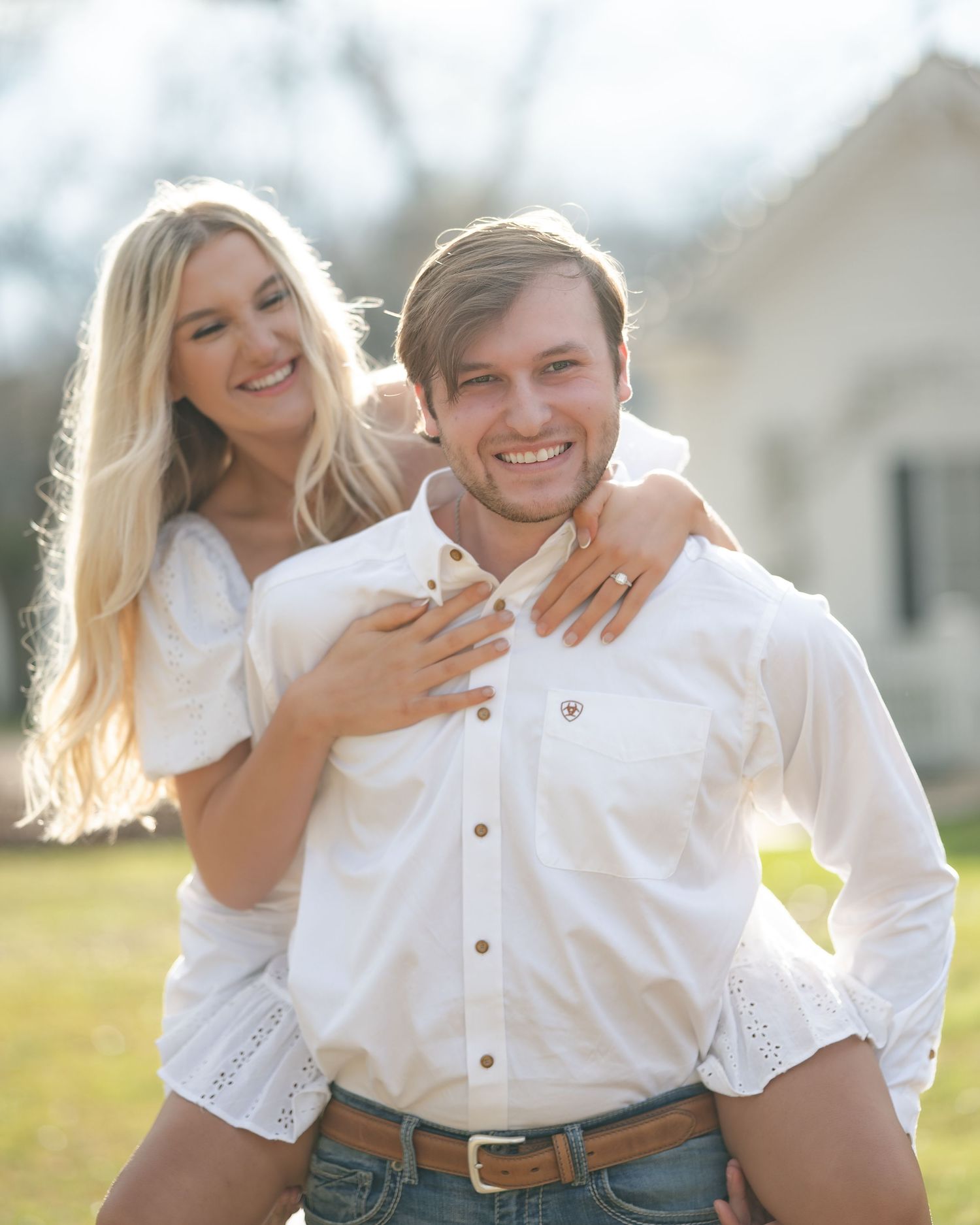 A playful couple in matching white shirts laugh and embrace while taking casual outdoor photos.