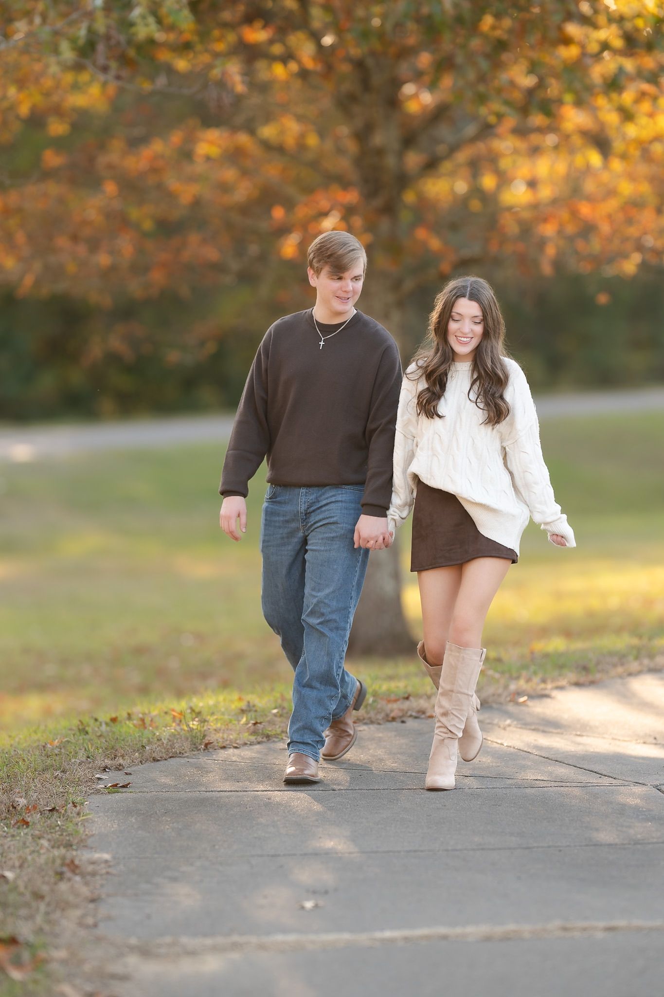 A couple walks together on a path surrounded by golden autumn foliage on a sunny afternoon.