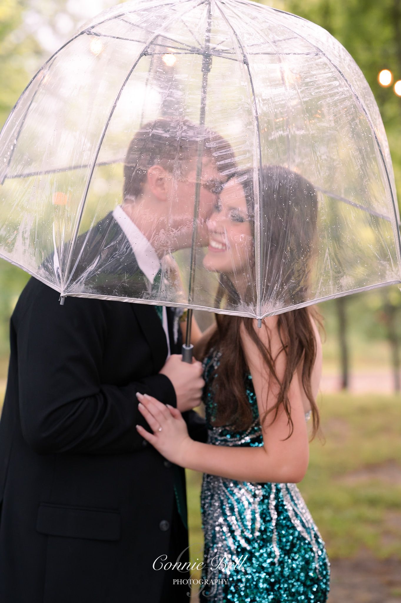 Couple sharing romantic moment under clear umbrella in formal attire.
