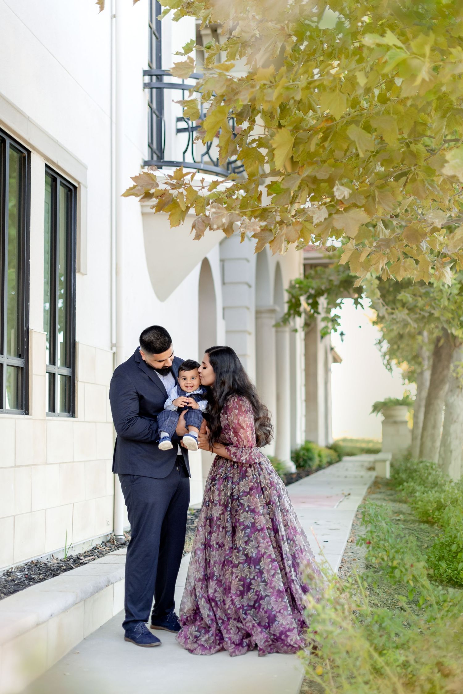 Intimate family moment captured outside modern building with elegant formal wear.