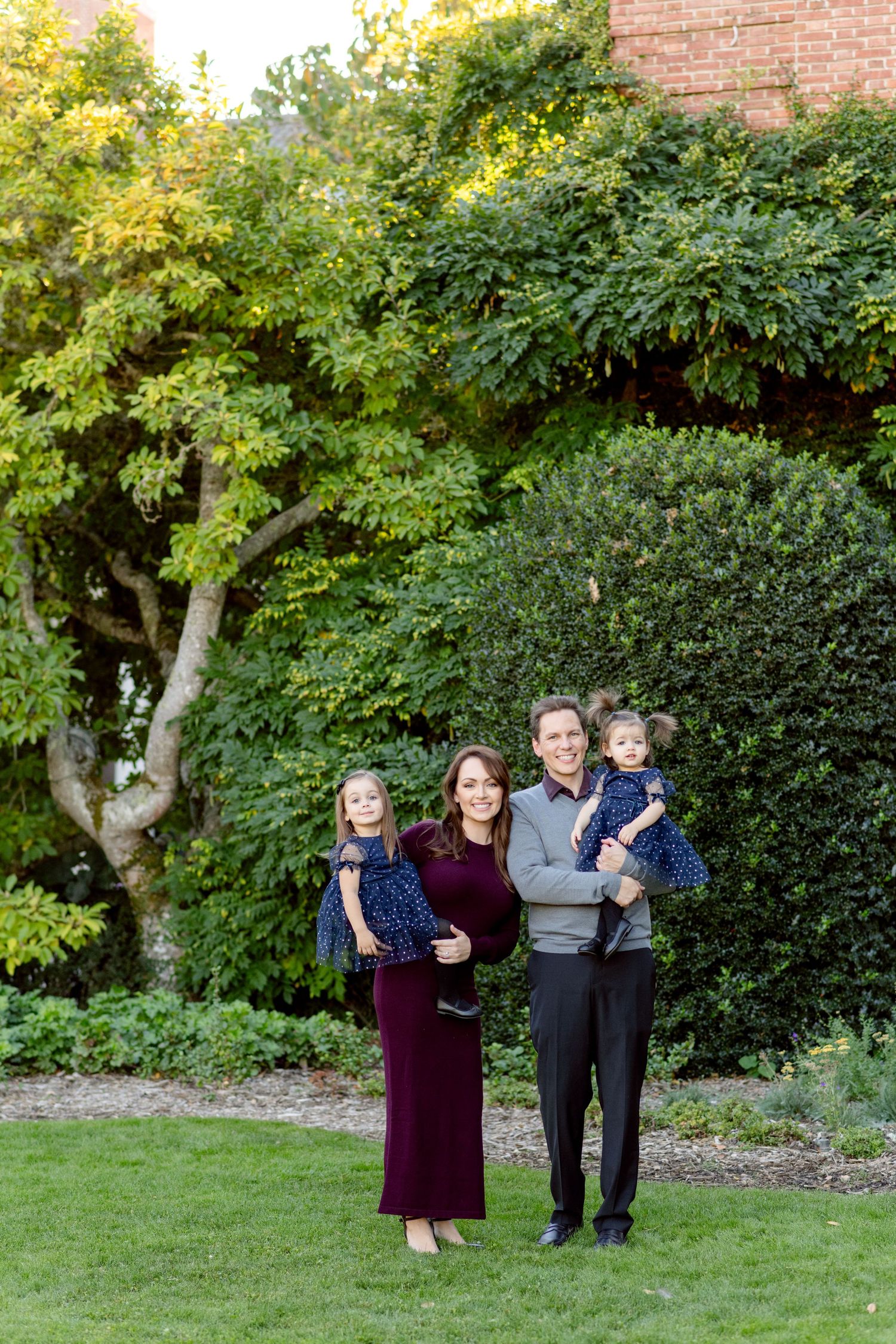 Family of four posing together in lush garden setting.