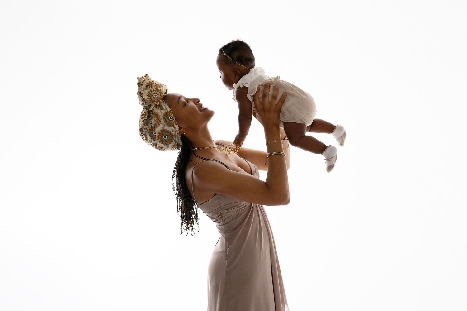 Parent lifting child playfully in graceful silhouette against white background.