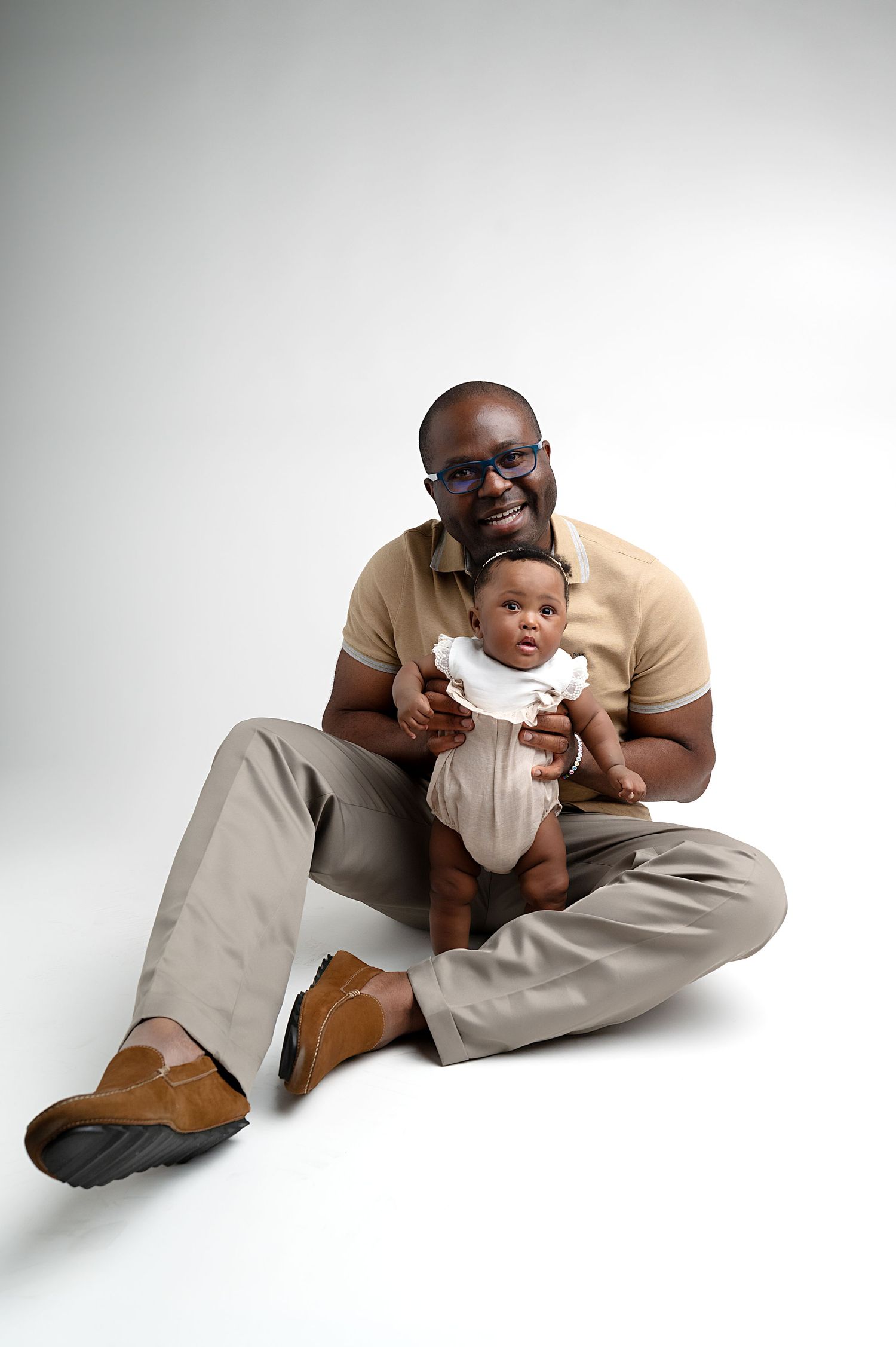 Parent and baby sharing joyful moment while sitting on white floor.