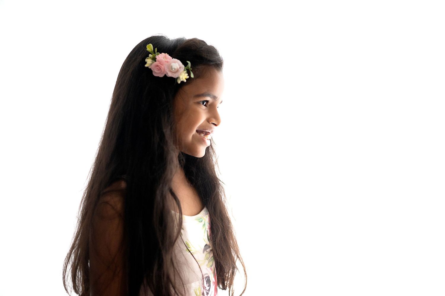 Side profile of person with long dark hair and floral accessory against white background.