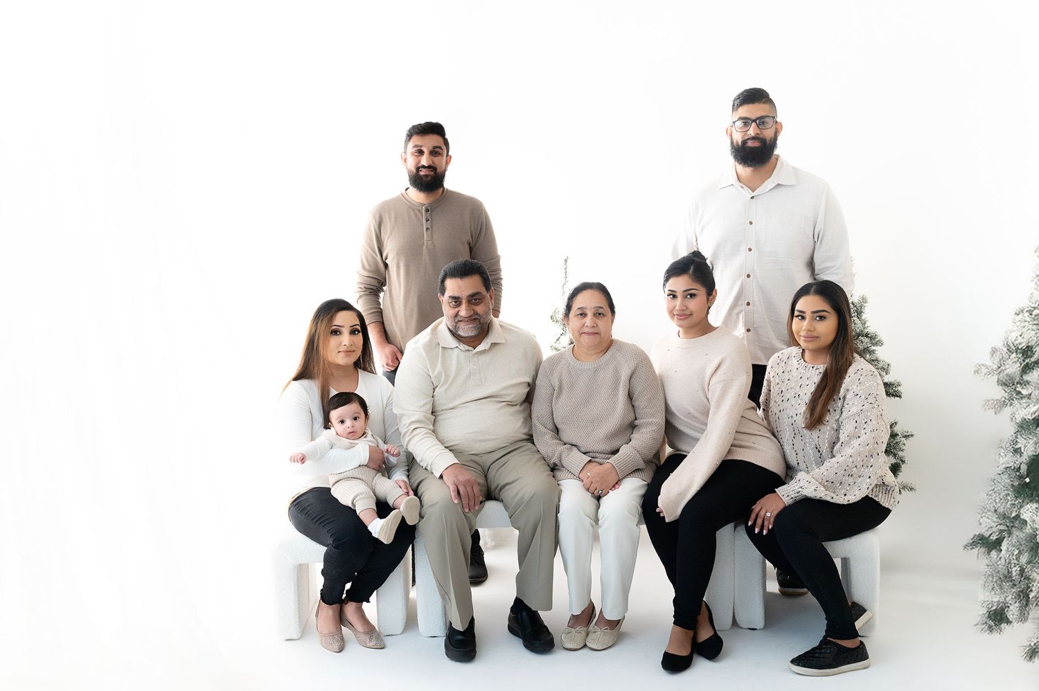Large family group wearing coordinated neutral colors posing together for a portrait on white background.