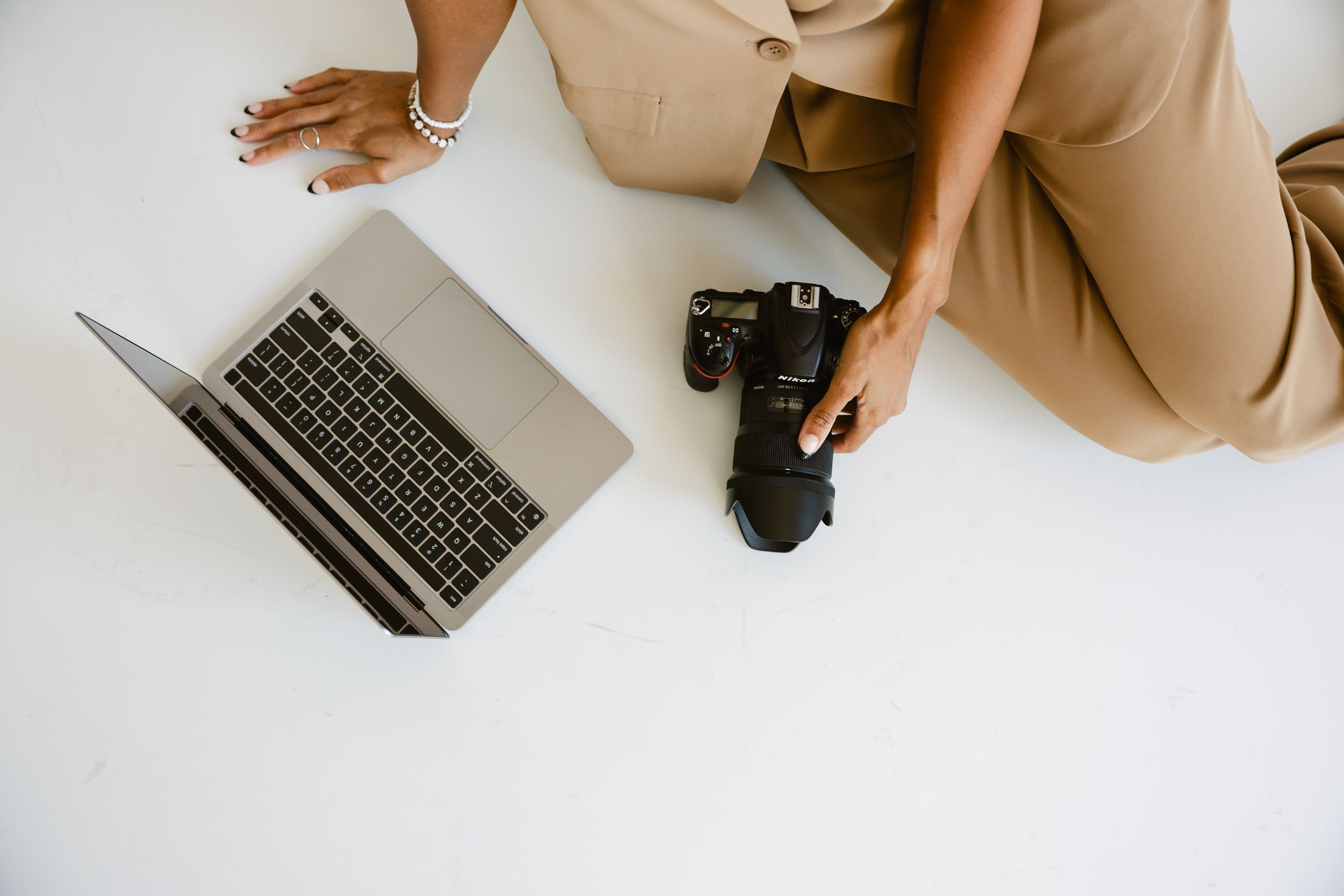 Overhead view of a photographer sitting on white floor holding a DSLR camera next to an open laptop during branding session.